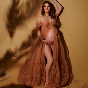 Femme enceinte avec une robe de tulle beige sur du sable et à l'ombre d'épis de blé sur fond beige