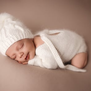 Nouveau-né endormi paisiblement sur un coussin moelleux, habillé d’un bonnet et grenouillère en alpaga doux et blanc 