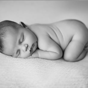 Photo de bébé en noir et blanc allongé sur le ventre en petit cocon laissant place à la douceur intemporelle de bébé