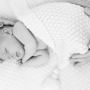 photo en noir et blanc de bébé endormi avec douceur entouré des mains de ses parents