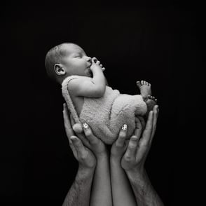 photo de bébé sur fond noir avec les main de ses parents