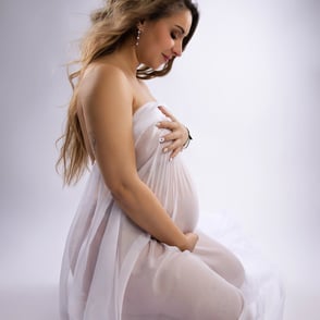 beaucoup de douceur dans cette photo de grossesse qui est assise au sol et portant un voile blanc transparent