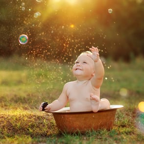 photo d’un bambin heureux dans un bassine et des bulles de savon dans un décor naturel dans les champs