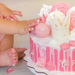 photo d’un bambin fête son premier anniversaire avec un smash cake aux couleurs douces et ses petites mains dans le gâteau