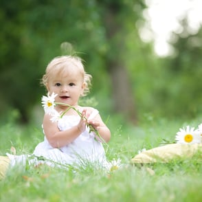 Portrait joyeux d’un bambin souriant, assis dans l’herbe avec une fleur à la main, capturé en pleine expression de bonheur