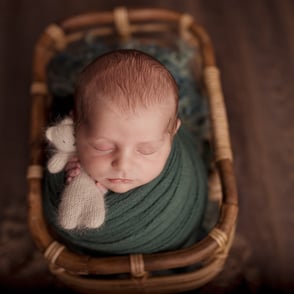 Photo de bébé endormi, emmailloté dans un wrap tenant un doudou dans ses petites mains tout en douceur