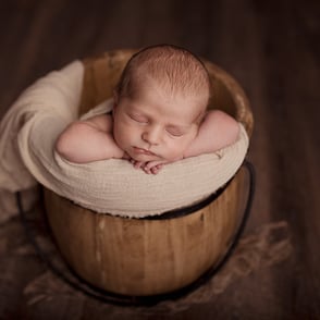 Portrait de bébé endormi dans un joli sceau en bois et recouvert d’un wrap beige