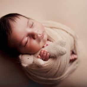 Photo de bébé endormi dans un wrap croisé laissant dépasser ses petits pieds et ses petites mains avec un doudou apaisant