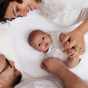 photo de bébé au centre tenu par ses parents de chaque côté