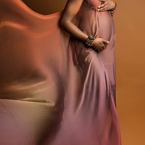 photographie de grossesse d'une femme de couleur sur fond brun portant un voile en robe brun irisé pour la mettre en valeur