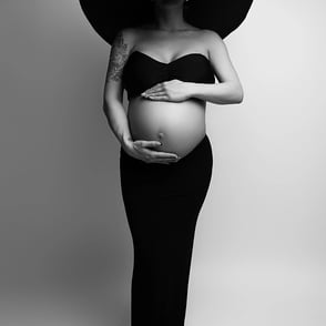 tableau de grossesse portant une longue jupe noir, chapeau noir et top noir