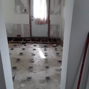 Entryway floor renovation with exposed joists and grid of adjustable pedestal supports for subfloor levelling