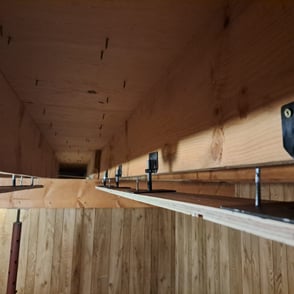 Adjustable metal brackets installed between wood joists for precision ceiling levelling in basement renovation