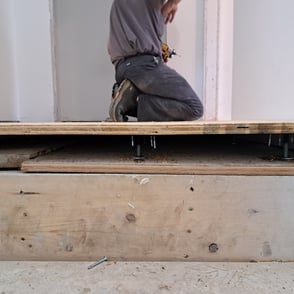 Contractor installing raised plywood subfloor using adjustable pedestals during residential floor levelling project