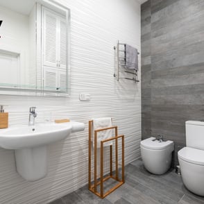 Baño con ducha de obra, mampara de cristal y revestimiento cerámico gris oscuro.