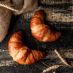 Two croissants on a dark wooden surface.