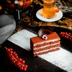 A slice of chocolate layer cake with a decorative chocolate piece on top, red currants on the side.