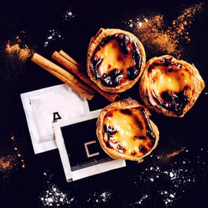 Three Portuguese egg tarts with a caramelized top next to cinnamon sticks.