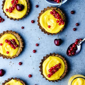 Multiple lemon tarts with red currants on top.