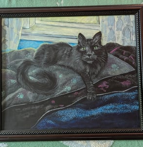 Cherry oak framed arcrylic portrait painting of a long haired black cat with very green eyes laying in his blanketed bean bag