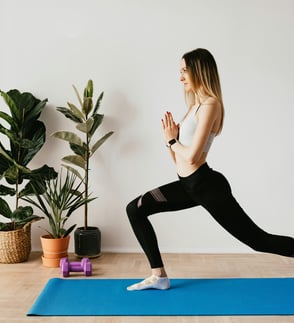 Mujer realizando una postura de zancada con las manos juntas durante una clase de pilates online ofrecida por Yarkeey.