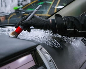 Nettoyage de l'habitacle d'un véhicule avec un pinceau et un produit moussant