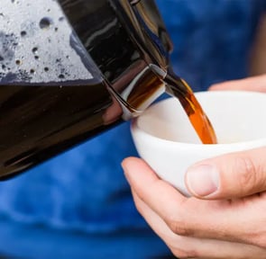a person is pouring a cup of coffee into a cup