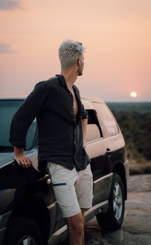 a man standing next to a car watching the african sun