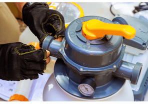 Image of a pool tech with gloves on inspecting a pool filtration system
