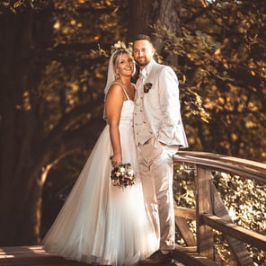 Brautpaar in eleganter Hochzeitskleidung auf einer Holzbrücke umgeben von Bäumen
