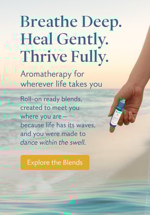 a person holding an essential oil roller bottle by the ocean