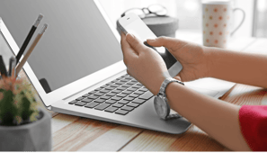 Enquadramento de uma pessoa olhando um celular frente à um notebook