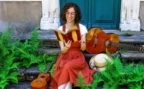 musicienne en train de lire un livre/a woman in a red dress reading on stairs with guitar beside her