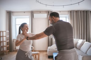 Pareja adulta sonriendo y haciendo un ejercicio de baile en su sala de estar.