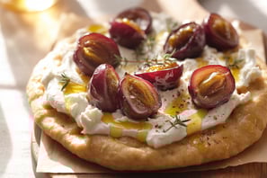 a pizza with grapes and cheese on a wooden board