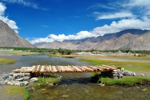 a wooden bridge over a river with a mountain in the background
