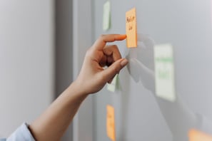 A hand posting a sticky note on a whiteboard during an ideation session