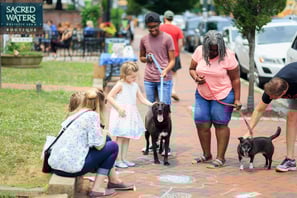 a group of people standing around a dog on a sidewalk