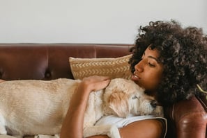 woman laying on couch hugging a dog on her chest