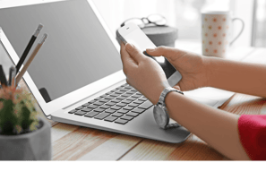 Enquadramento de uma pessoa olhando um celular frente à um notebook