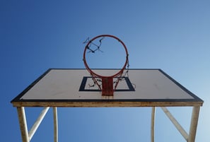 Low‑angle view of a weathered basketball hoop mounted on a white backboard against a clear blue sky