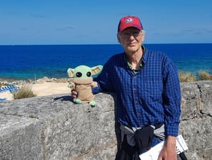 Man standing against low wall holding a little green companion with ocean in background