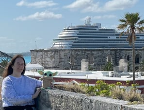 Woman standing by low wall holding a little green companion with cruise ship in background