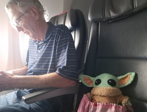 Man in airplane seat with a little green companion in seat next to him