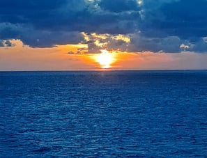 Deep blue ocean with orange sunset and deep blue clouds in sky