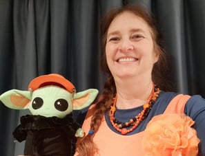 Woman wearing orange shirt holding a little green companion wearing an orange hat