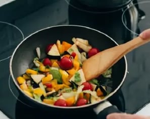 The image shows a stir-fry with bell peppers, tomatoes, and other vegetables being stirred in a pan.