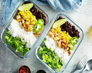  Two meal prep containers with rice, chicken, beans, corn, and greens.