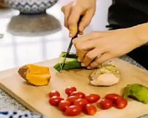 A person slicing a cucumber on a cutting board with various fresh ingredients.