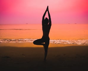 Silhouette of a woman practicing yoga on the beach at sunset